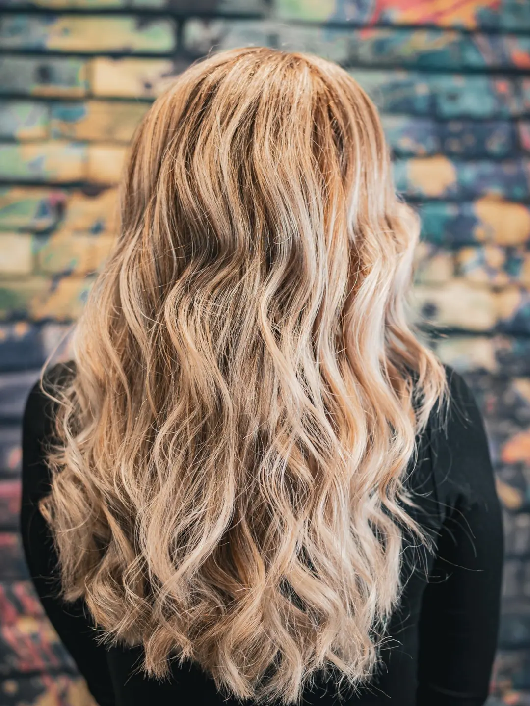 Dlhé vlasy s blond balayage pred farebnou tehlovou stenou